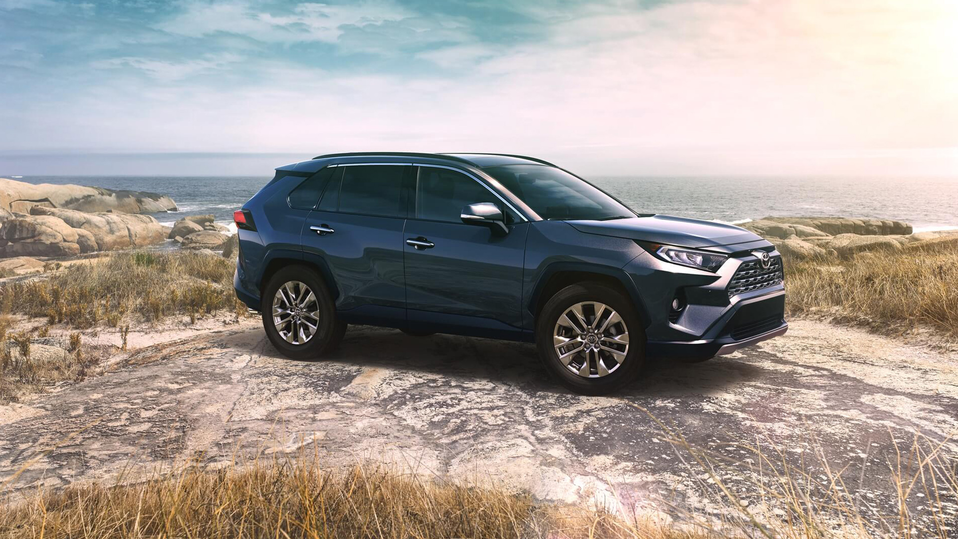 A black Toyota RAV4 parked on a rocky coast, the ocean stretching into the background.