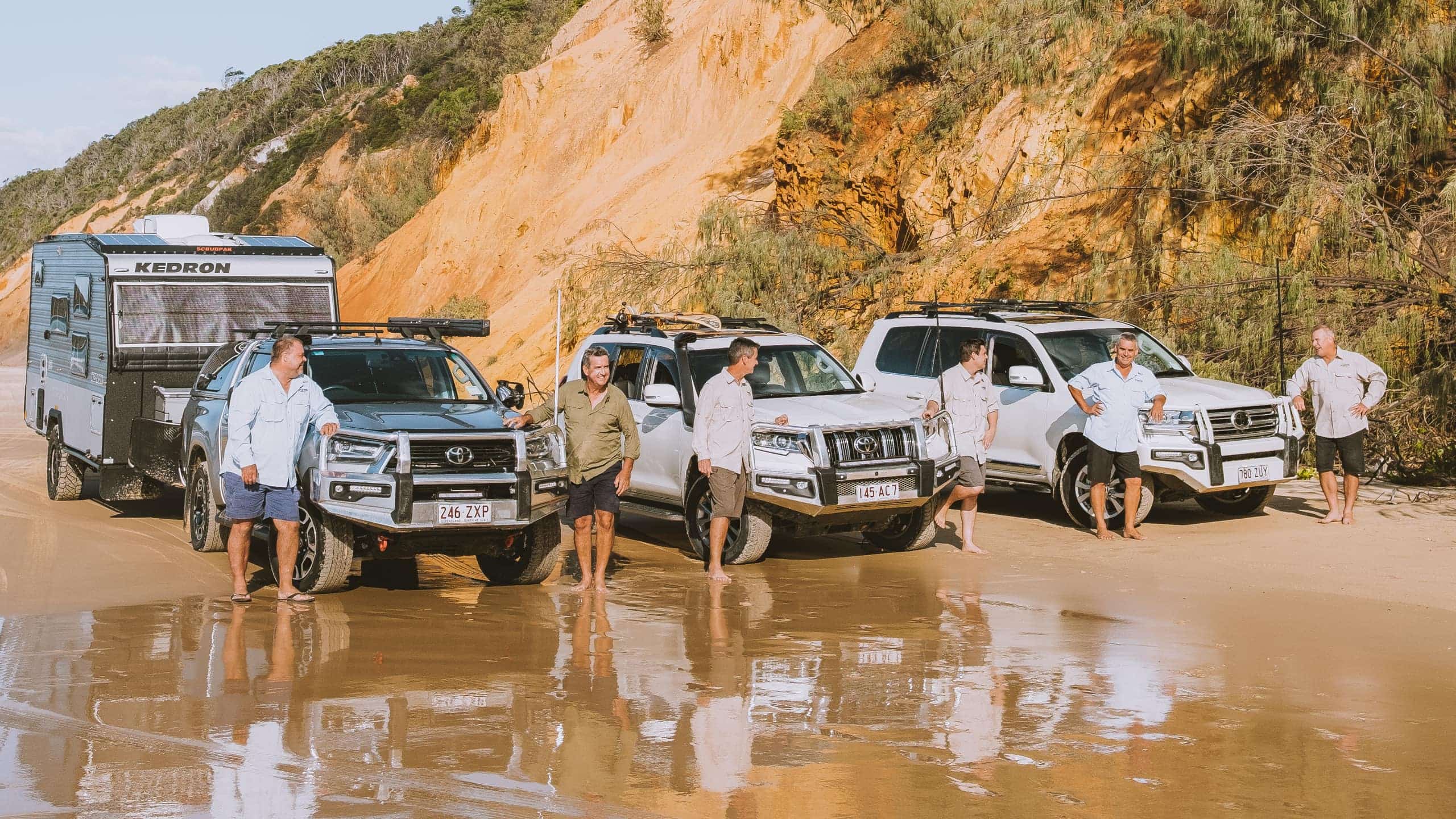 The Gall Boys family, all six men standing with their Toyotas, each one parked on the edge of a flooded road. From left to right, Hilux, LandCruiser Prado J150, and a LandCruiser 300.