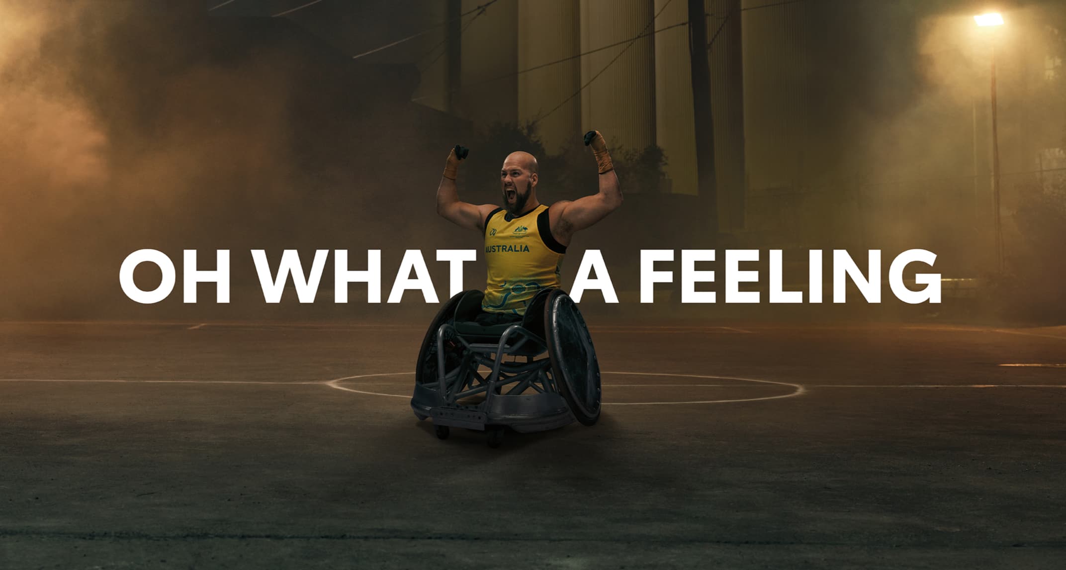 Australian Paralympian wheelchair rugby player Ryley Batt, posing with his arms flexed upwards, on a moodily lit, foggy basketball court at night. ‘OH WHAT A FEELING’ is superimposed into the image.