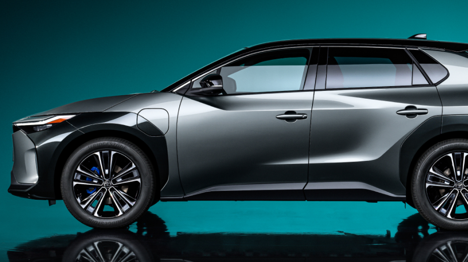The side profile of a dark grey Toyota bZ4X against a blue-green backlit wall.