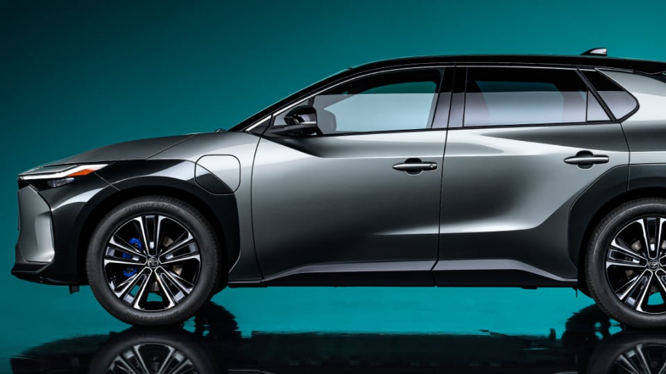 The side profile of a dark grey Toyota bZ4X against a blue-green backlit wall.