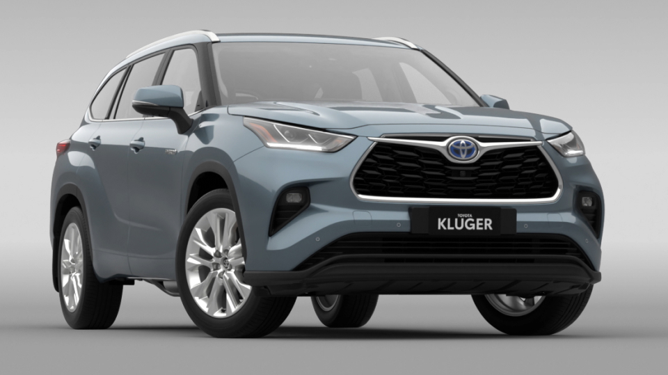 A blue-grey Toyota Kluger driving down a modern inner-city street, greenery jutting out from between buildings.