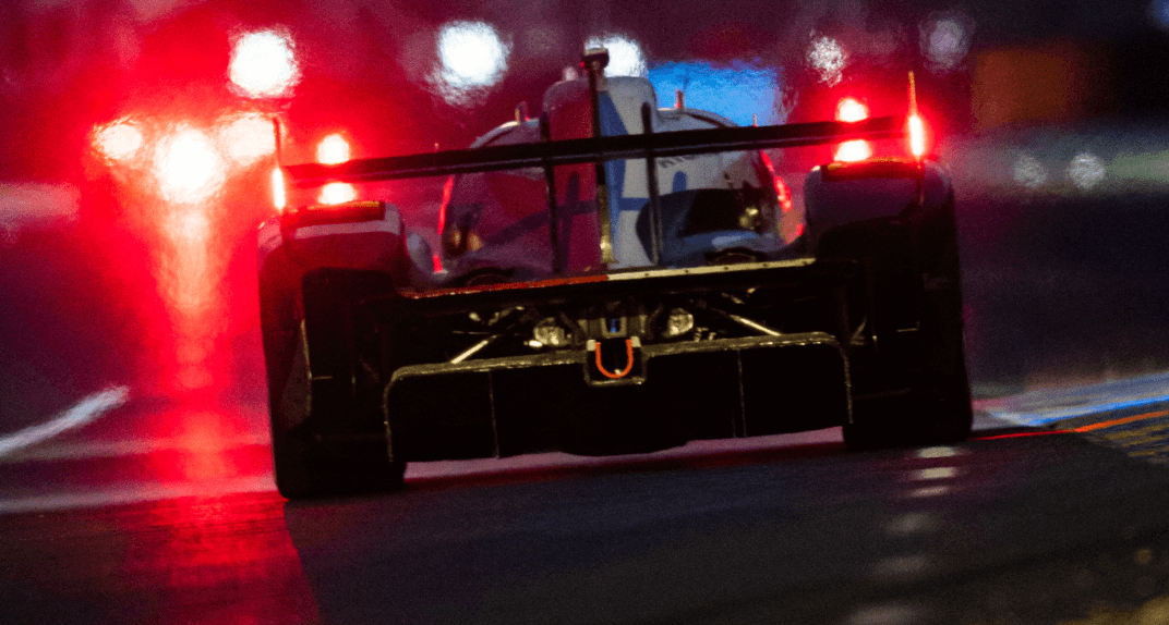 A Toyota race car seen from behind on a track at night, with its bright red tail lights glowing.