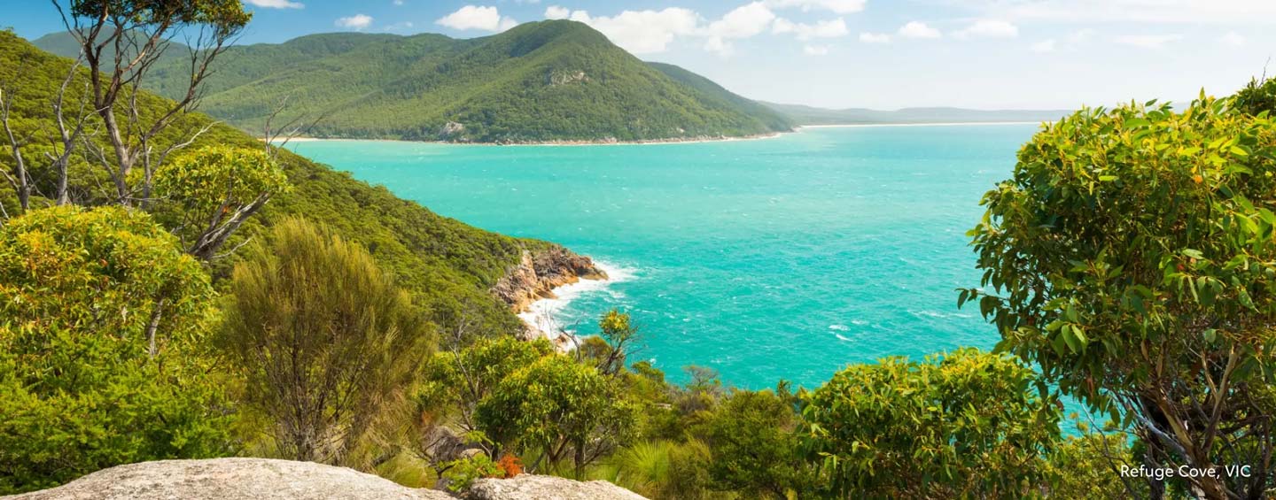 A rocky outcrop overlooking the blue waters of Refuge Cove in Victoria, surrounded by a lush green coastal forest.