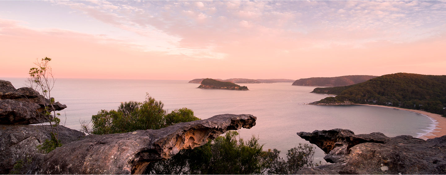 A rocky cove along NSW’s Sapphire Coast during dusk, the sky hues of peach and dusty blues as the sun sets out of frame.