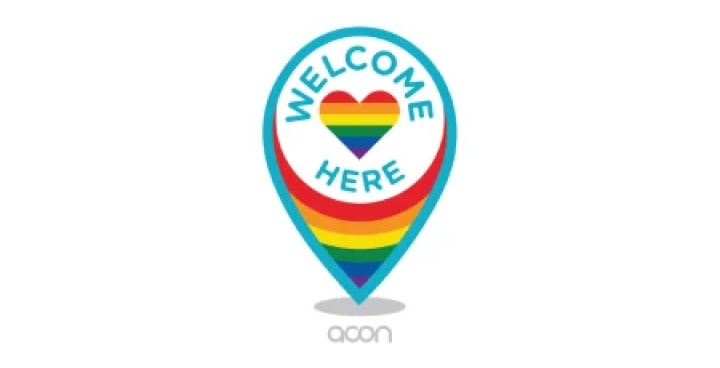 The Welcome Here logo; a location pin shape with a strong aqua coloured outline, with the words “Welcome here” inside, surrounding a rainbow coloured heart.