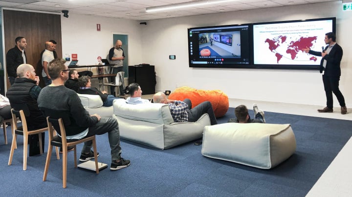 Toyota employees in a lounge with two large TV screens and comfy couches, intently watching a presentation.