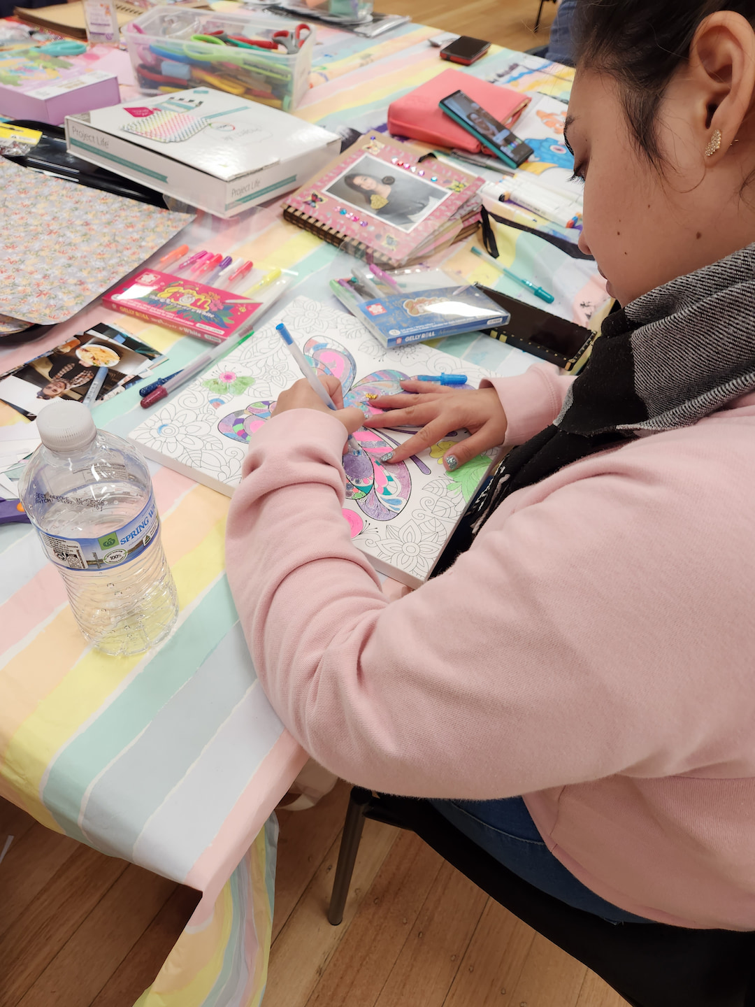 A young adult filling out a colouring stencil of a butterfly using a range of vivid gel pens.