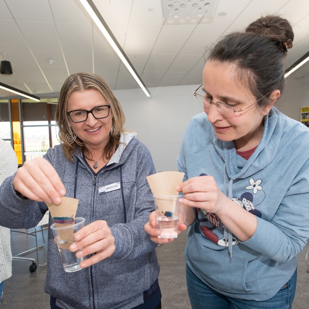 Two female primary school teachers participate in Fizzics Education, practising in an experiment involving plastic cups and liquids. This experiment is one they’re learning to take back and show their students. 