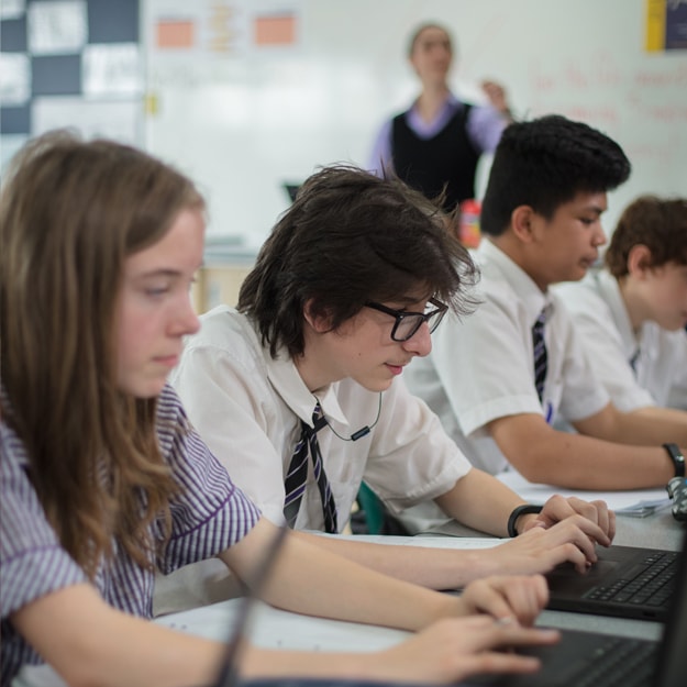 Students sat in a row at desks observing a demonstration in a learning environment.