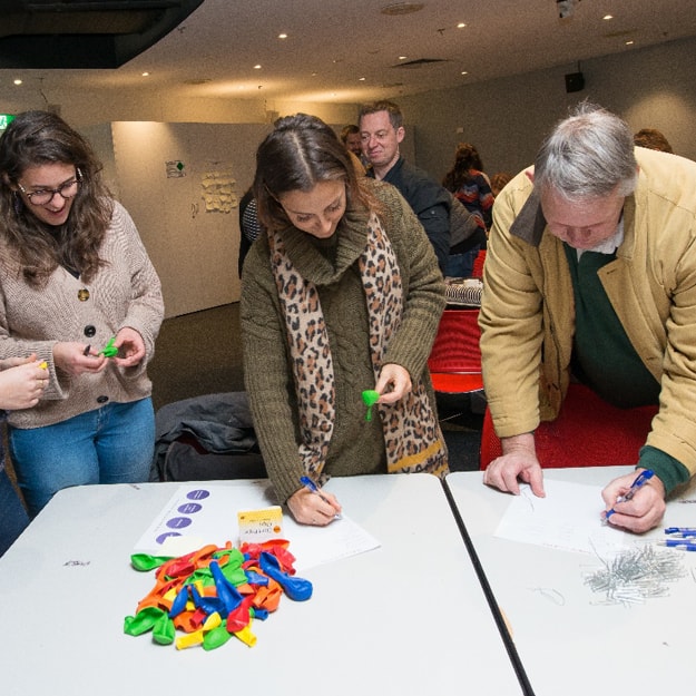 Arrivals at a Questacon event, writing down their names on stickers to wear, and each picking up a balloon on arrival, presumably for an icebreaker game. 