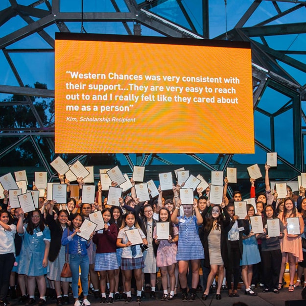 A large group of students on stage at The Edge, Federation Square in Melbourne, holding up Western Chances scholarship certificates in celebration.