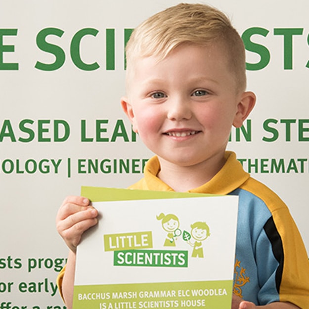 A young primary school boy with platinum blonde hair and blue eyes, proudly holding up a Little Scientists certificate.
