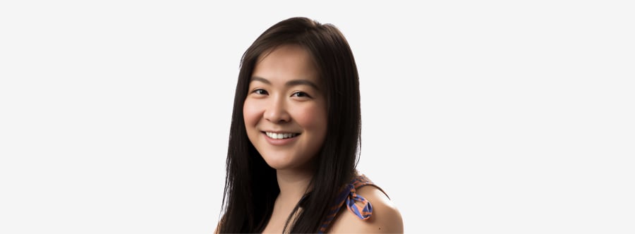 A woman with long straight black hair and rosy cheeks, beaming happily smiling softly in front of a bright white backdrop.