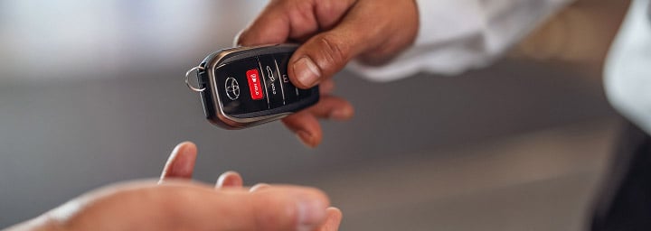 A woman stands next to a Toyota Dealer, holding a digital tablet and accompanying pen, the door of a blue Toyota ajar.