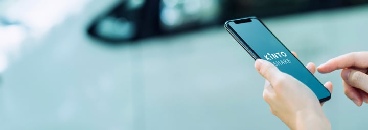 A person standing by the side of a road, accessing the Kinto app on their mobile device.