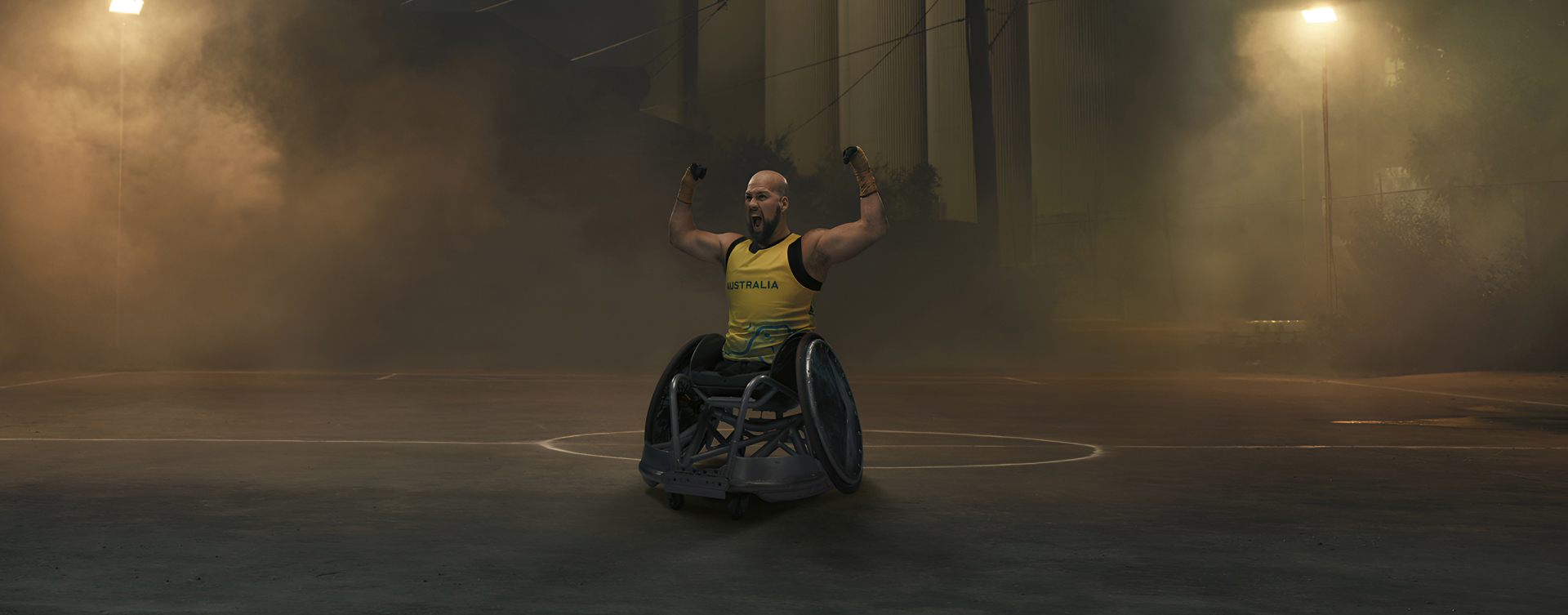 Australian Paralympian wheelchair rugby player Ryley Batt, posing with his arms flexed upwards, on a moodily lit, foggy basketball court at night.
