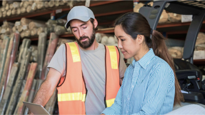 A man in high-visibility work gear and a woman in office workwear, together in a storage warehouse.