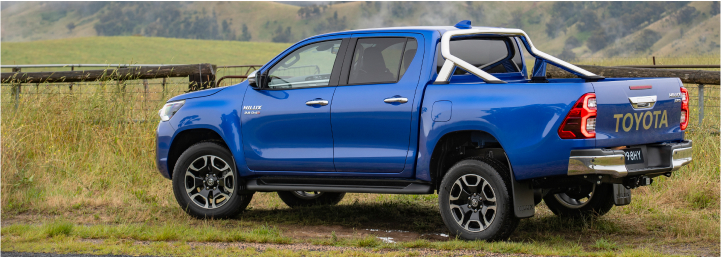A blue Toyota HiLux parked in front of a wooden fence, overlooking a green misty valley.