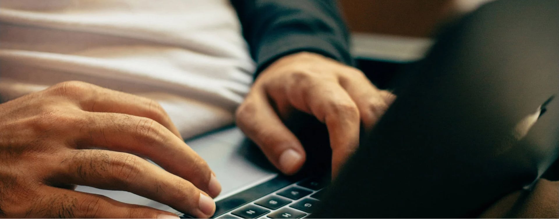A man resting his hands on the surface of a silver laptop, his right index finger touching the trackpad to navigate.
