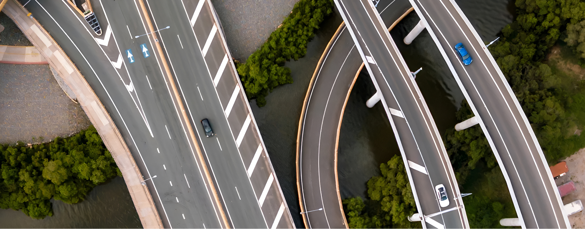 An aerial view of layered highways, suspended over a river lined with lush, green trees.