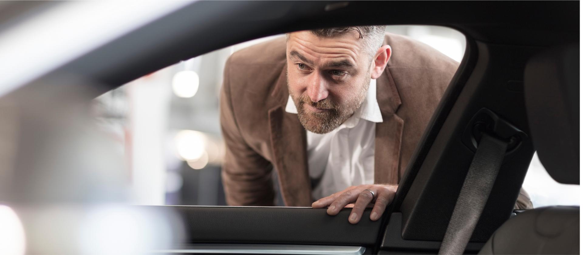 A man in a brown suede jacket looking into the open front passenger window of a Toyota vehicle.