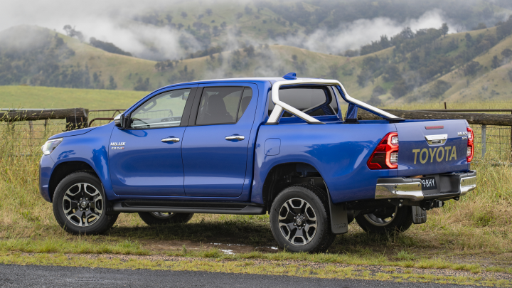 A blue Toyota HiLux parked facing a grassy paddock amongst misty mountains, in the Australian countryside.