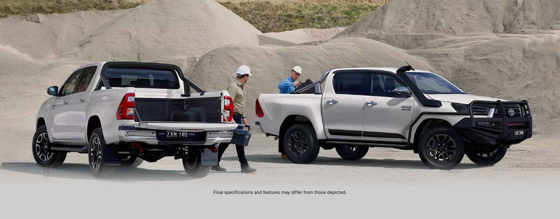 Two white Toyota HiLux vehicles parked among the grey mounds of an outback quarry. Two workers with white hard hats are collecting toolboxes from the trays of their vehicles.