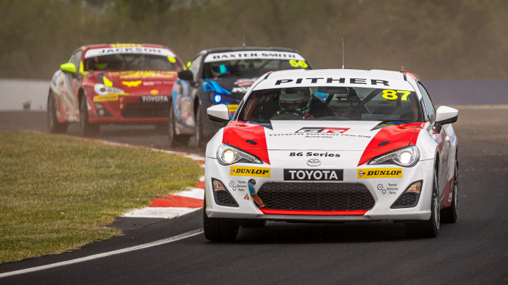 Three Toyota G R 86s in racing livery competing on a winding track during the Bathurst 1000. Smoke hangs in the air.