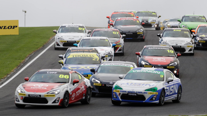 A large group of Toyota G R 86s in racing livery spill over the hill of the track as they compete in the Phillip Island 500.