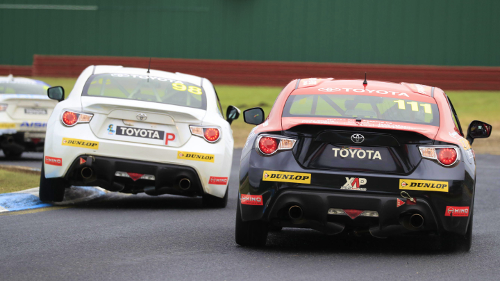 Competing Toyota G R 86s in racing livery leaning to their right side as they corner a bend during the Sandown 500.