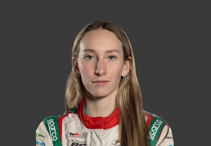 A headshot of professional T G R A driver Alice Buckley in a red, white and green racing suit against a grey background.