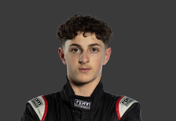 A headshot of professional T G R A driver Pip Casabene in a black, white and red racing suit against a grey background.