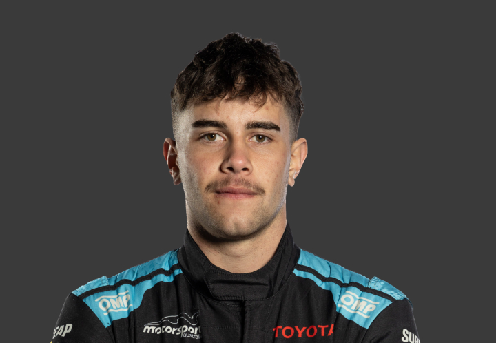 A headshot of professional T G R A driver Kade Davey in a black and light blue racing suit against a grey background.