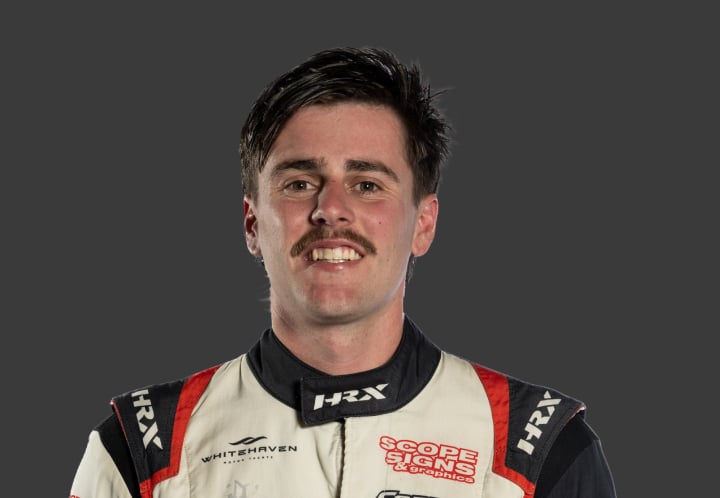 A headshot of professional T G R A driver Jordan Freestone in a white, black and red racing suit against a grey background.