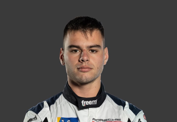 A headshot of professional T G R A driver James Lodge in a white and black racing suit against a grey background.