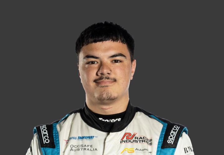 A headshot of professional T G R A driver Byron Lutelu in a blue and white racing suit against a grey background.