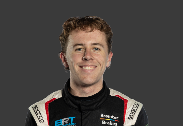 A headshot of professional T G R A driver Clay Richards in a black, white and red racing suit against a grey background.