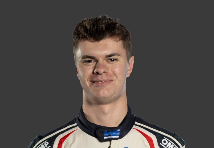A headshot of professional T G R A driver William Seal in a white, navy blue and red racing suit against a grey background.