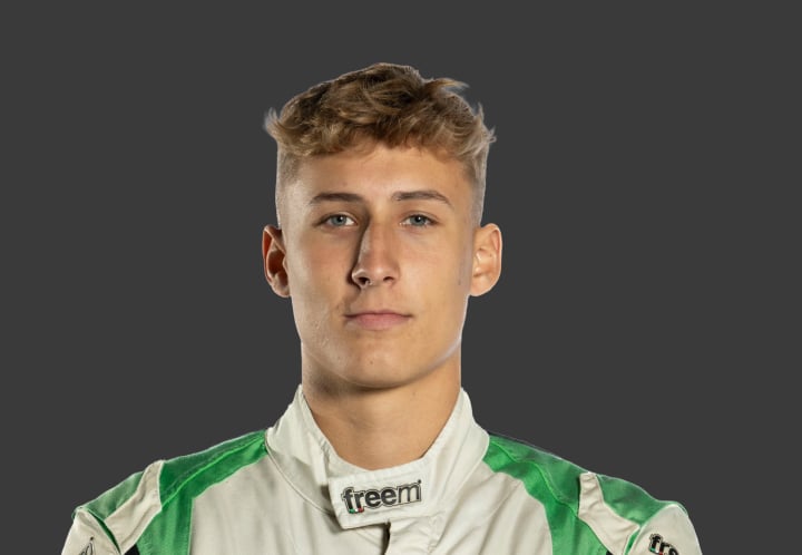 A headshot of professional T G R A driver Hugo Simpson in a white and green racing suit against a grey background.
