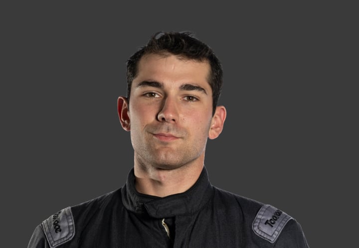 A headshot of professional T G R A driver Brock Stinson in a black and dark grey racing suit against a grey background.