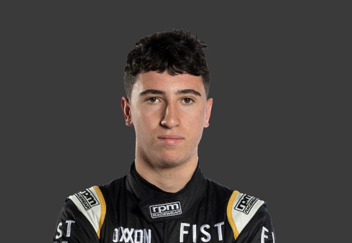 A headshot of professional T G R A driver Max Walton in a black, white and yellow racing suit against a grey background.