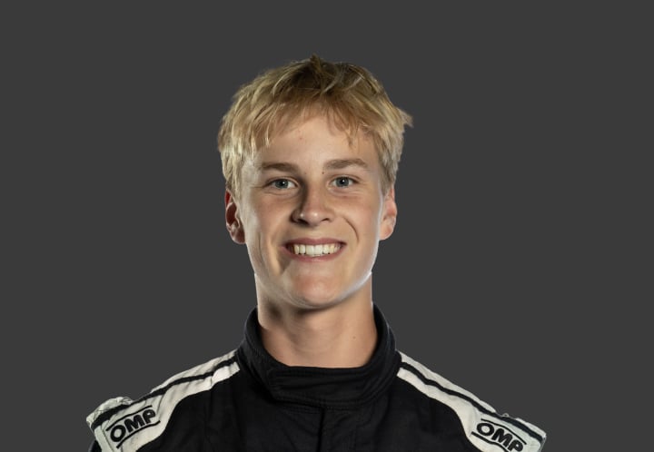 A headshot of professional T G R A driver Oli Wickham in a black and white racing suit against a grey background.