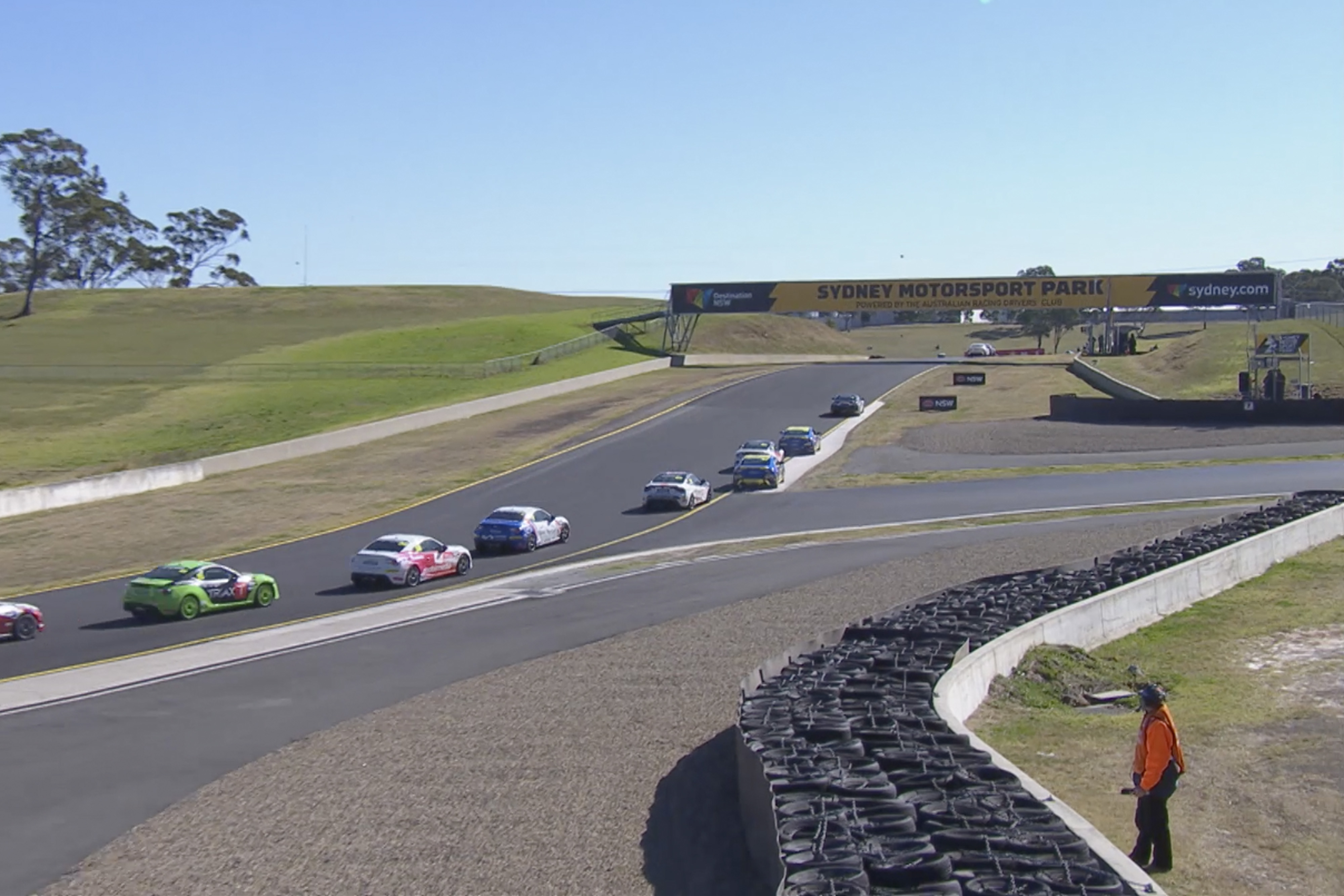 Toyota G R 86s in racing livery competing at Sydney Motorsport Park on a clear sunny day. Bundles of tyres line the track.
