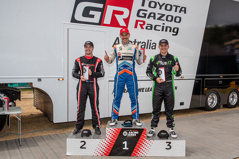 Professional racing drivers on a T G R A 86 Racing Series podium. First place (middle) is Luke King, second Place (left) is Zane Morse, third place is George Gutierrez.
