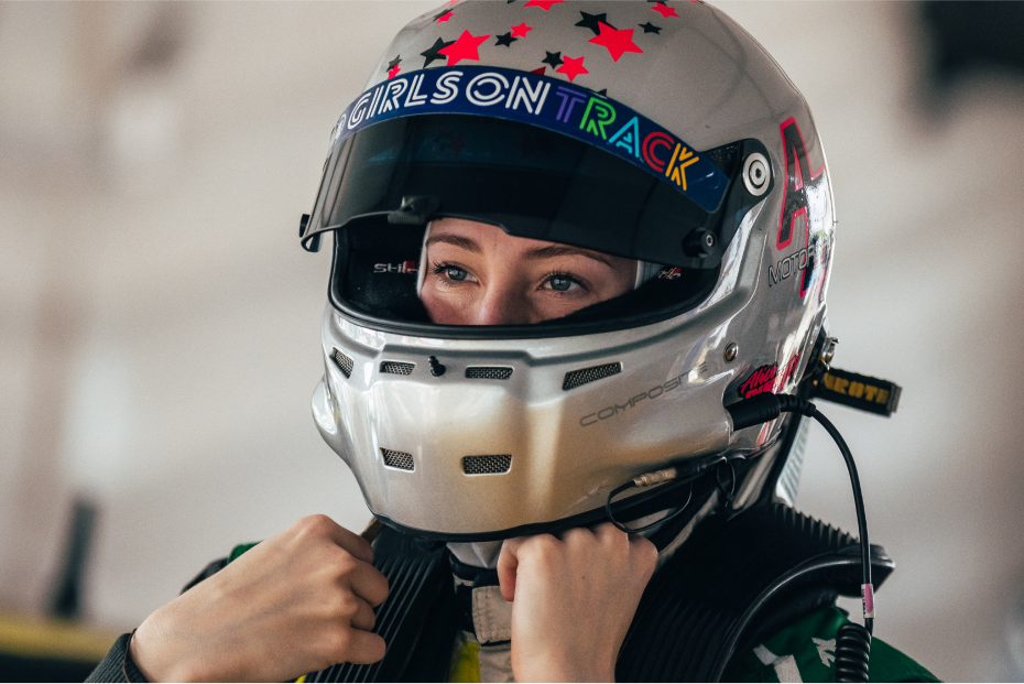 Professional racing driver Alice Buckley adjusting her helmet. The top of her visor says 'GIRLS ON TRACK'.