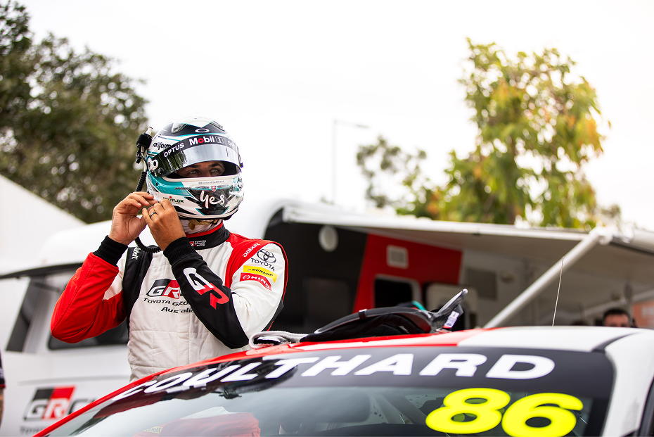 Professional racing driver Fabian Coulthard adjusting his helmet as he stands next to a white Toyota GR 86 in racing livery.
