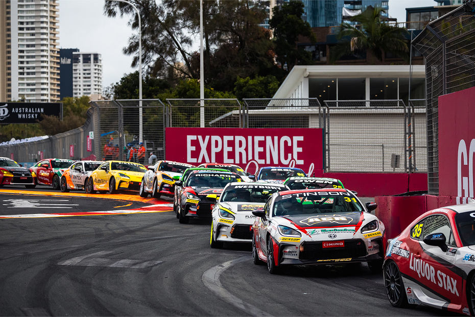 Twelve Toyota G R 86s in racing livery make a tight turn one after another while competing on a racetrack in Surfers Paradise.