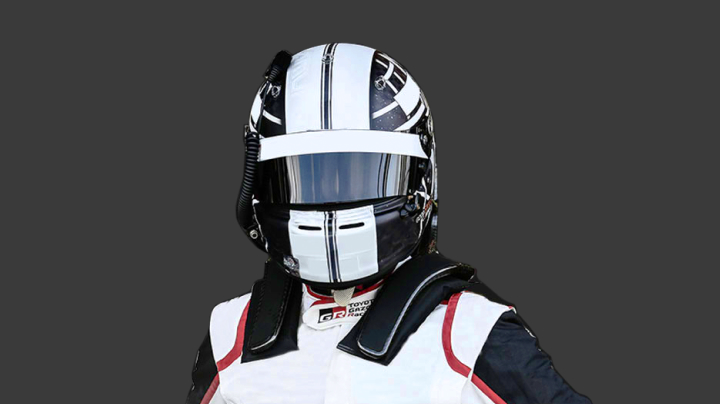 A headshot of a professional T G R A driver in a closed helmet with the visor down, in red, white and black racing suit against a grey background.
