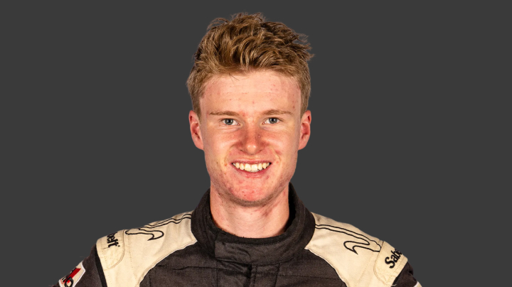 A headshot of professional T G R A driver Zach Bates in black and white racing suit, against a grey background.